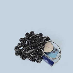 Interior detail of black beaded handbag with silver ring handles holding cosmetics