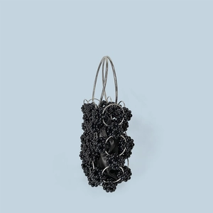Detail of black beaded handbag with metallic ring handle on light blue background