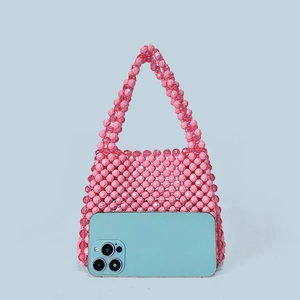 Macro shot of handmade beaded handbag in vibrant pink showing mini size relative to smartphone