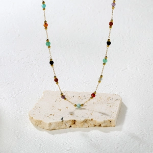 Ensemble collier en acier inoxydable doré et pierres naturelles sur socle en travertin
