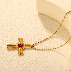 Collier croix en acier doré avec un zircon rouge carré sur un fond minimaliste chic