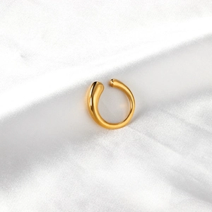 Gros plan d'une bague ouverte dorée irrégulière sur un fond de soie blanche