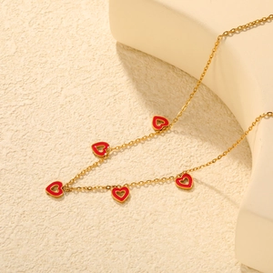 Detail of gold-plated necklace featuring five red enamel heart pendants on a fine chain