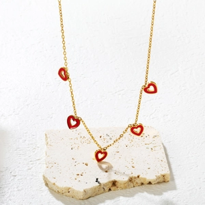 Detail of gold chain necklace with five red enamel heart pendants on a stone base