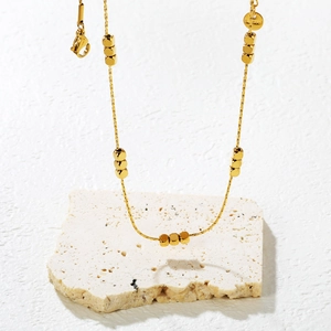 Minimalist gold stainless steel necklace with cube beads on a textured stone base