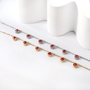 Close-up of gold and silver anklets with pink round rhinestones on a wavy white surface