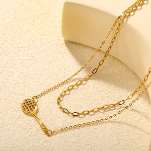 Collier double rang doré avec pendentif raquette de tennis sur un support texturé