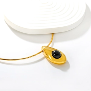 Macro di collana a serpente dorata con ciondolo a goccia nero su fondo bianco