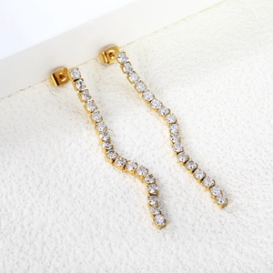 Detail view of gold tassel earrings with clear cubic zirconia on textured background