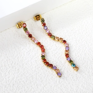 Detail of long wavy gold earrings with colorful rhinestones on a white textured background