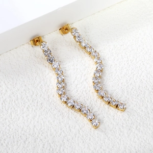Close-up of gold-plated wavy tassel earrings with crystal zircon inlay on white props