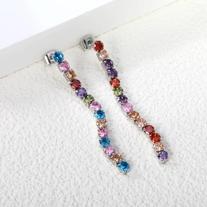 Close-up of long tassel earrings with multicolored zircons on a white display stand
