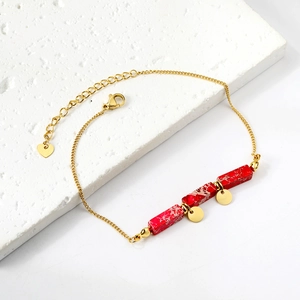 Detail of gold ankle chain featuring red stone rectangles and heart charm pendant