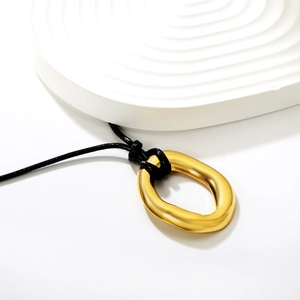 Pendentif ovale doré irrégulier avec cordon noir sur fond de texture ondulée blanche