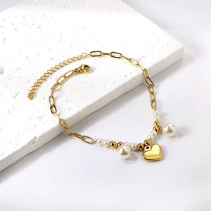 Detail of golden stainless steel heart charm and white pearl anklet on a white stone