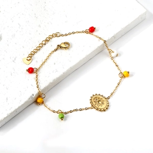 Detail of gold ankle chain featuring colorful beads and a sun pendant on white stone