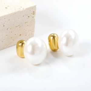 Elegant gold bead and large white oval pearl stud earrings on a textured stone display