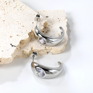 Detail of silver C-shape earrings with inlaid round clear zircon on white stone