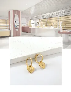 Détail de boucles d'oreilles cœur dorées avec texture soleil et cristal sur plaque de pierre