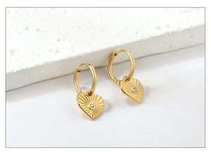 Détails de boucles d'oreilles cœur dorées avec texture rayonnante et cristal central