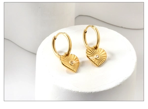 Détail de boucles d'oreilles cœur doré avec texture rayon de soleil et pierre