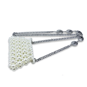 Close-up of handmade pearl mini bag featuring unique embossed metal charms on silver chain