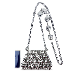 Detail of silver beaded mini bag with chain strap and sunburst coin emblem near a lipstick