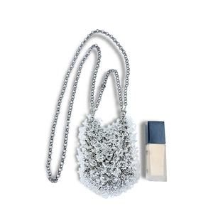 Mini acrylic beaded evening bag with silver chain strap shown next to foundation for size