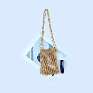 Close-up of golden metal mesh phone bag with fine chain strap on a white background