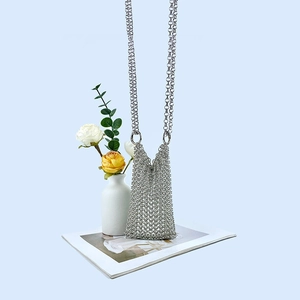 Silver metal chainmail crossbody bag hanging next to a white vase and flowers