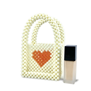 Detail of handmade beaded pearl mini handbag with red heart pattern next to a small bottle