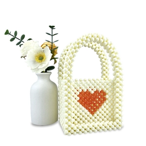 Detailed view of a handmade pearl beaded mini bag with a red heart pattern on white