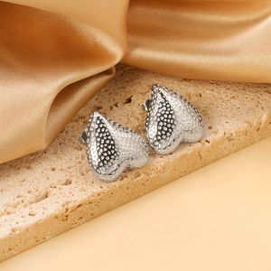 Silver heart studs with hammered texture on a stone background with gold silk