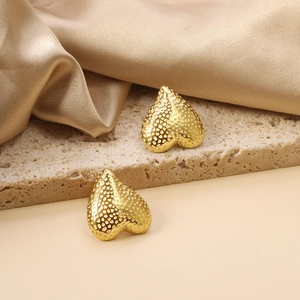 Gold heart-shaped stud earrings with hammered texture on a stone and satin surface