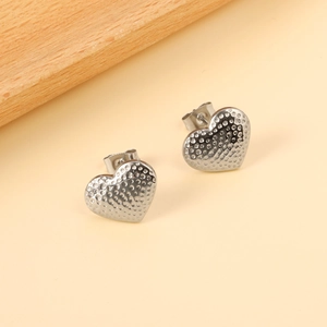Minimalist silver heart earrings with hammered metal texture in a flat lay scene