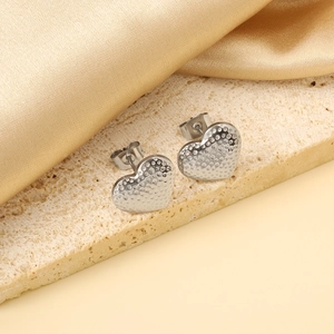 Macro shot of silver heart studs with textured hammered finish on silk and stone