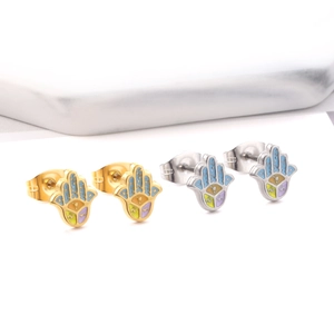 Macro view of gold and silver Hamsa hand stud earrings with colorful enamel on marble