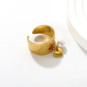 Detail of 18K gold ring featuring bark texture, a white pearl and a heart charm