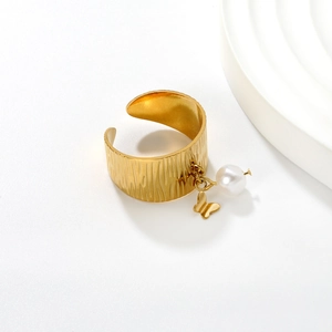 Detail of 18K gold open ring with butterfly charm, pearl pendant and bark texture surface