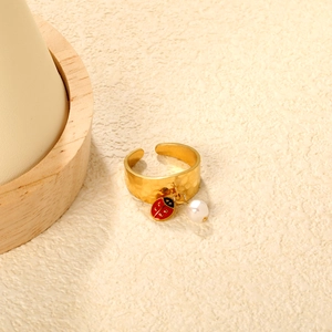 Detail of 18K gold open ring featuring a hammer texture, enamel ladybug and white pearl