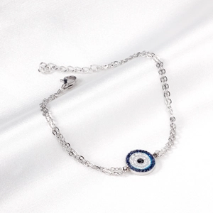 Close-up of a silver double-chain bracelet with a blue evil eye pendant on white silk