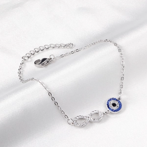 Detail of silver chain bracelet featuring a zircon infinity symbol and blue evil eye charm