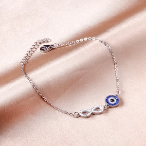 Silver infinity evil eye bracelet with blue stones and crystals on satin background