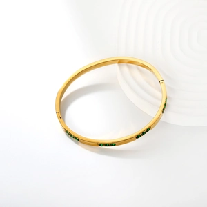 Gold-plated stainless steel bangle with inlaid emerald green stones on white background