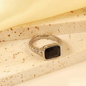 Macro shot of silver textured ring with a rectangular black gemstone on stone and silk