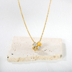 Polished gold four-leaf clover necklace with sparkling rhinestones on stone background