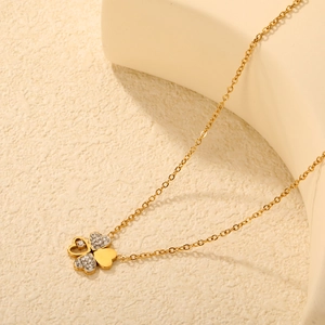 Elegant gold four-leaf clover pendant necklace with sparkling rhinestones on cream background