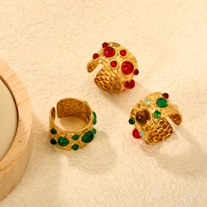18K gold plated wide open rings with red and green gemstones on beige textured surface