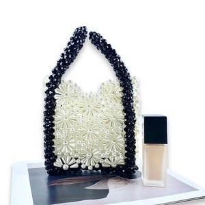 Detail showing handmade floral beadwork pattern on a woven white and black handbag