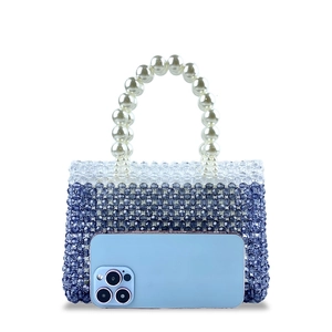 Detail of beaded handbag with blue gradient beads and large pearl handle next to a phone